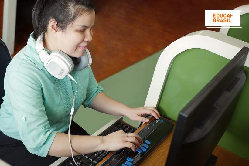 Funcionária com deficiência visual usando recuso de leitura em empresa acessível para pessoas com deficiência. Funcionária com deficiência visual usando recuso de leitura em empresa acessível para pessoas com deficiência.