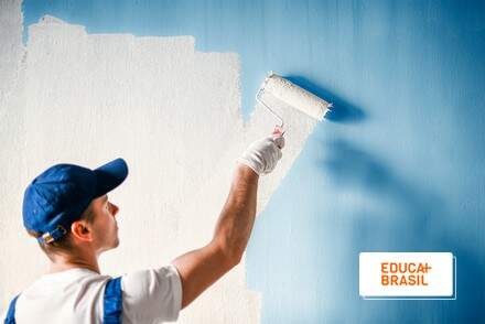 Pintor com rolo na mão pintando parede azul com tinta branca. Pintor com rolo na mão pintando parede azul com tinta branca.