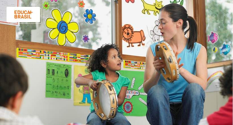 Professora tocando pandeiro e ensinando parlendas para criança. Professora tocando pandeiro e ensinando parlendas para criança.