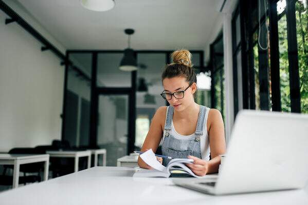 Estudante com livro na mão e com o notebook sobre a mesa. Estudante com livro na mão e com o notebook sobre a mesa.