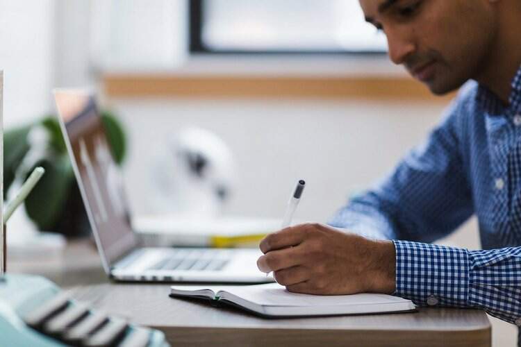 Homem estuda com notebook e caderno de anotações Homem estuda com notebook e caderno de anotações