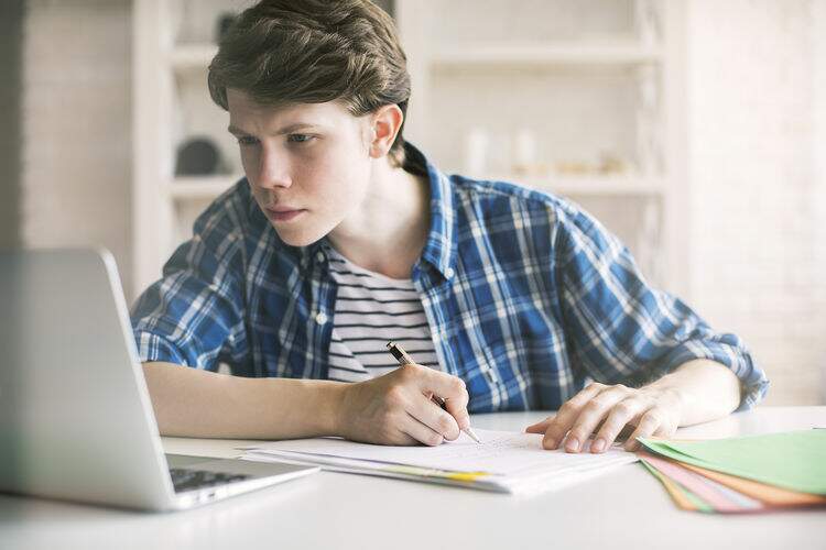 Estudante olhando o notebook e fazendo anotações