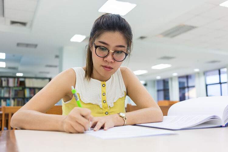 Menina de óculos sentada na mesa escrevendo Menina de óculos sentada na mesa escrevendo