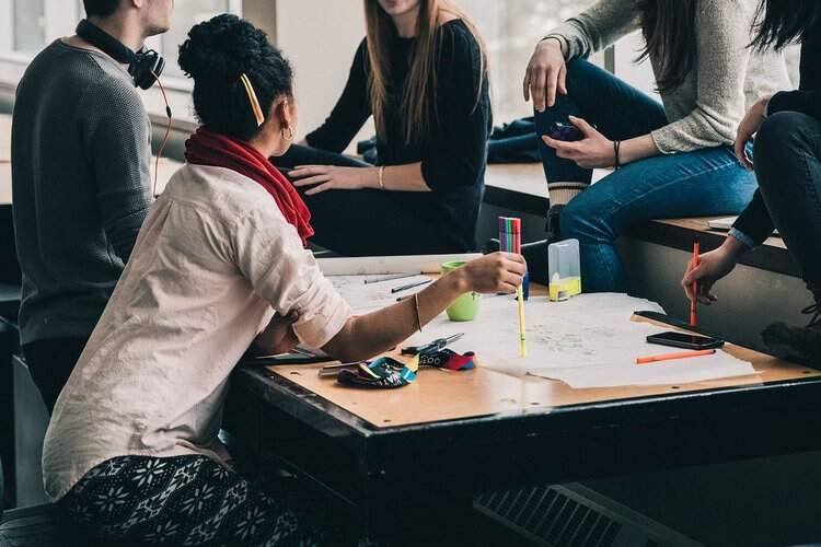 Jovens reunidos ao redor de uma mesa com canetas e papeis. Jovens reunidos ao redor de uma mesa com canetas e papeis.